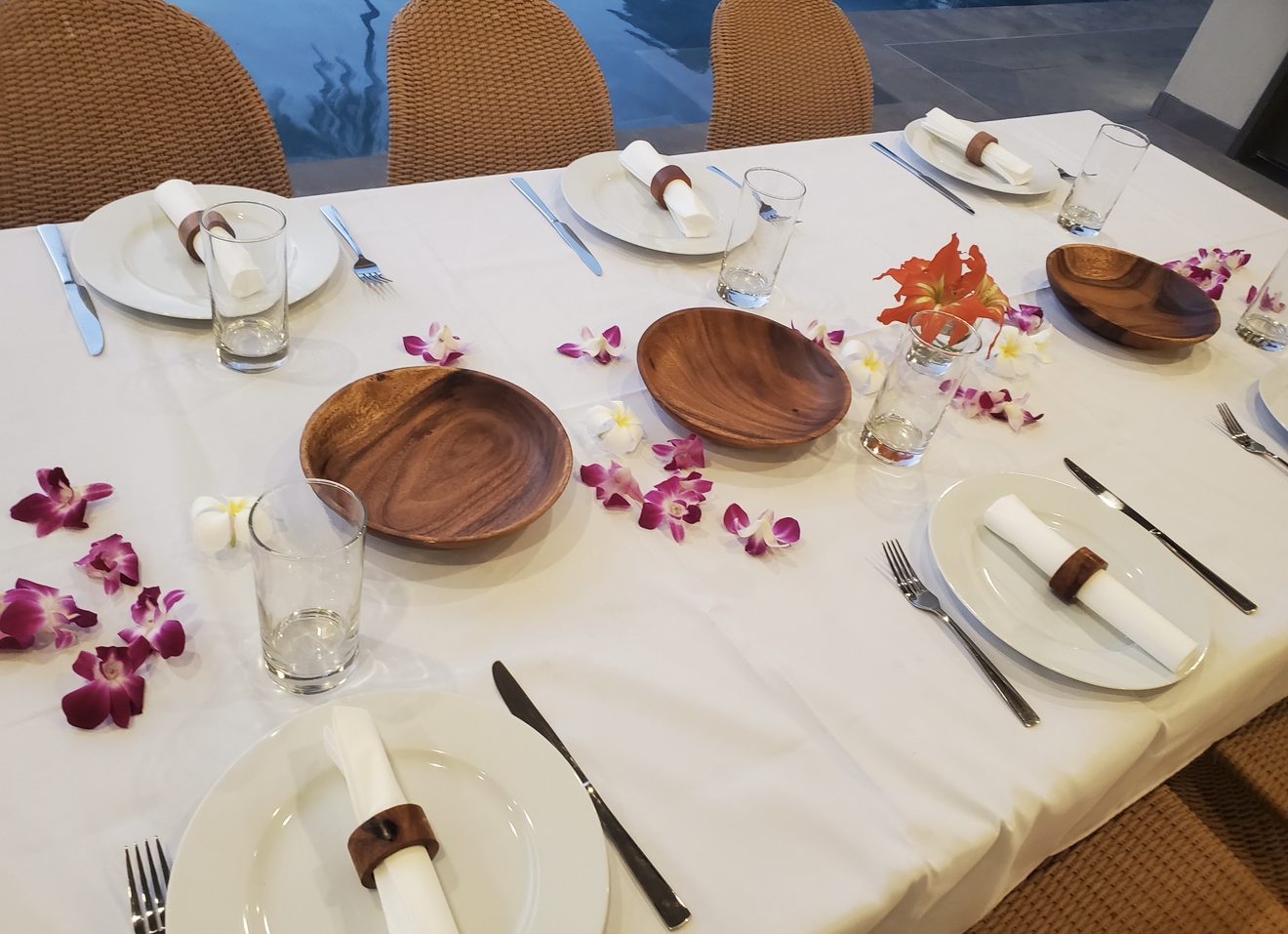 A white-linen table set with wooden bowls, napkin rings and orchid petals