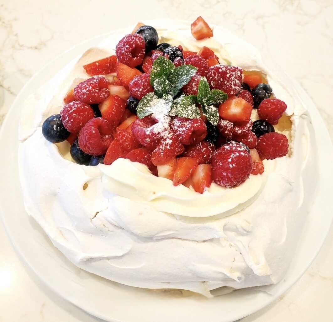 Pavlova topped with whipped cream and fresh berries