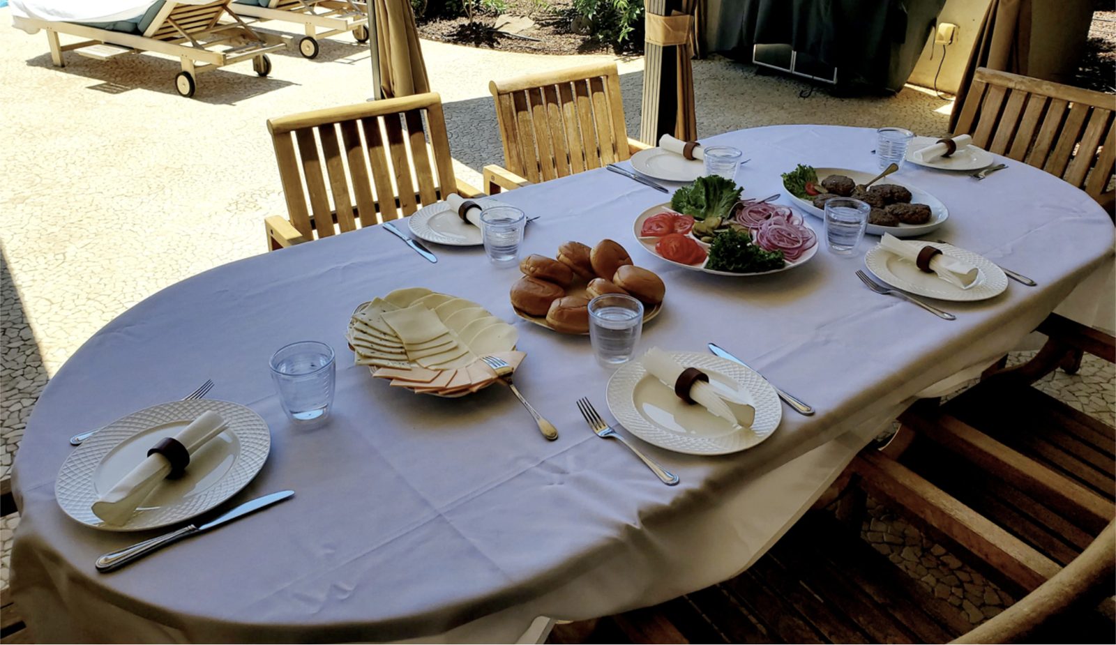 An outdoor table set for a burger lunch by the pool